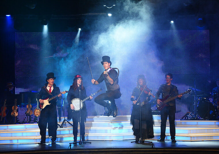 Live Musical Performance at The Dutton Inn Theater at The Dutton Inn | Branson Mo Musicians performing on stage with one jumping violinist at The Dutton Family Theater in at The Dutton Inn | Branson Mo