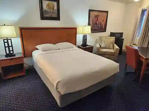 Well-lit guest room with a queen bed, two bedside lamps, armchair, desk, and framed artwork at The Dutton Inn | Branson Mo