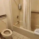 Clean guest bathroom with bathtub, shower curtain, toilet, and grab bars at The Dutton Inn | Branson Mo