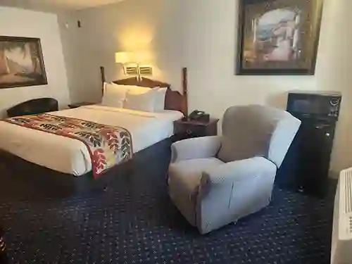 Cozy guest room with a king bed, armchair, nightstand, and framed artwork at The Dutton Inn | Branson Mo