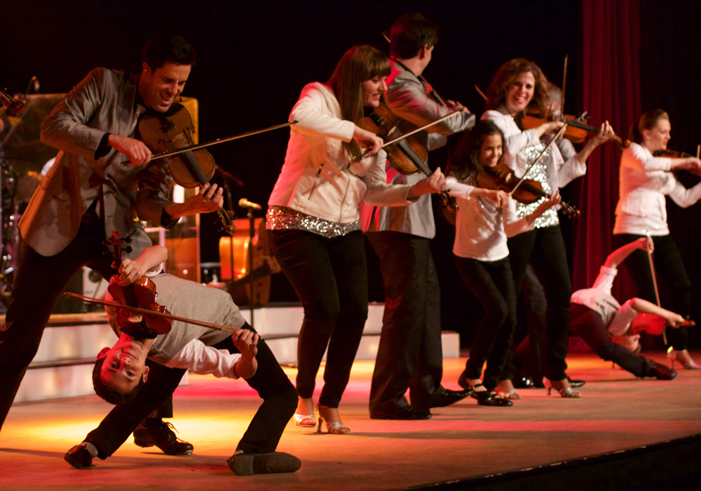 Group of musicians playing violins energetically on stage at The Dutton Inn in Branson Mo at The Dutton Inn | Branson Mo