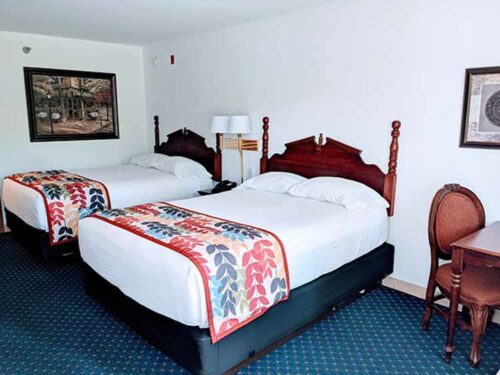 Two neatly made double beds with colorful quilts in a guest room at The Dutton Inn | Branson Mo