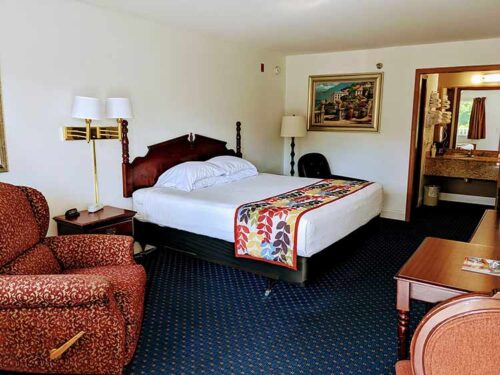 Spacious guest room with queen bed, patterned armchair, and vanity area at The Dutton Inn | Branson Mo
